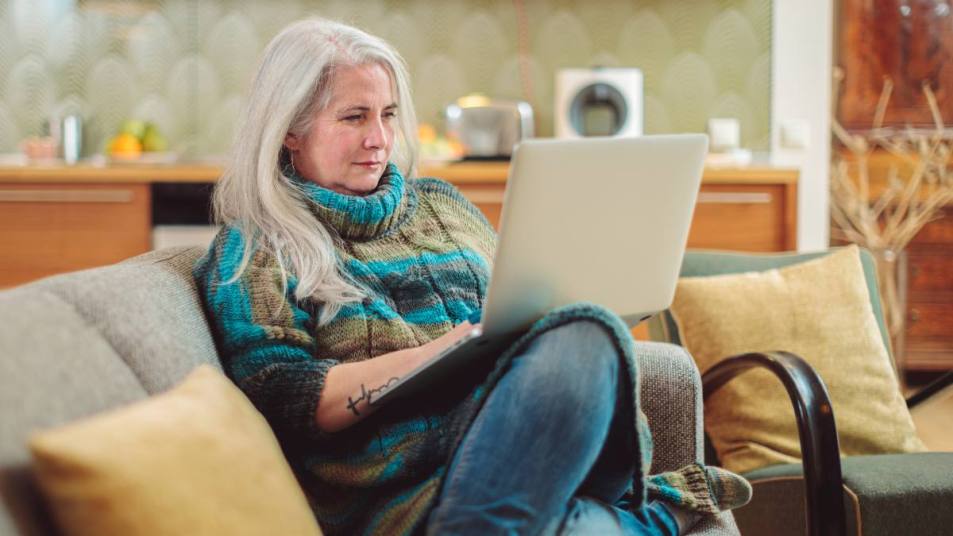 best jobs for women over 50 are things you can do at home, like this lady is doing on her couch.