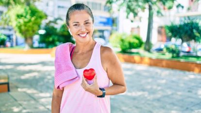 Woman outdoors wearing a towel on her shoulder and holding a red heart