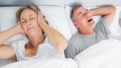A couple in bed with the woman covering her ears due to the man snoring