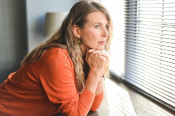 Woman with mildly concerned expression sitting looking out window for how to stop worrying about things you can't control