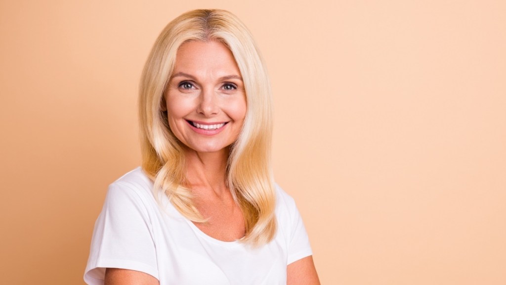 A blonde woman in a white t-shirt with a peach background