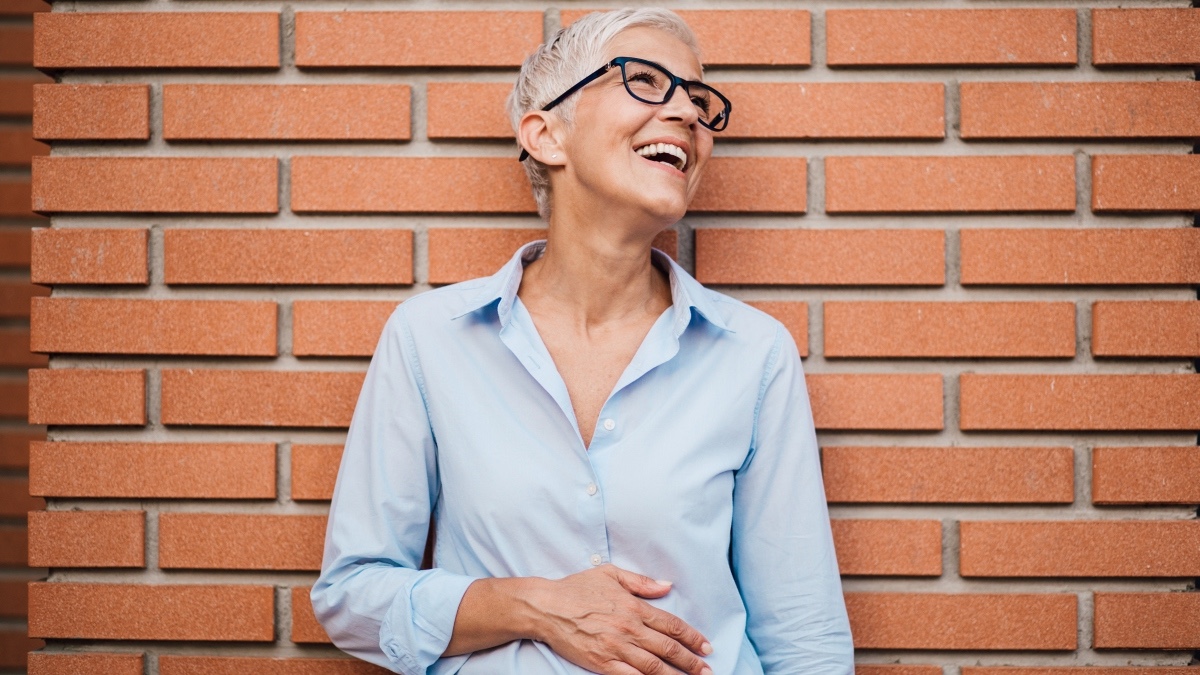 A mature woman against a brick wall with her hand on her stomach after losing lower belly fat