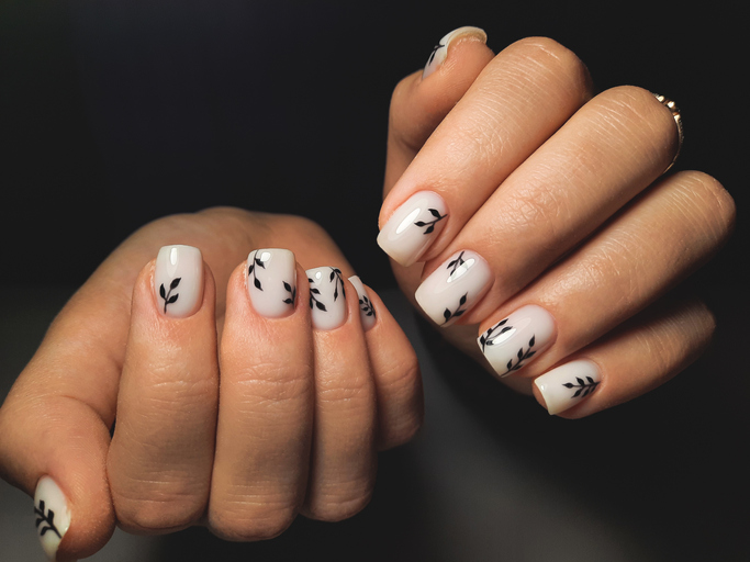 Short acrylic nails with milky white base and black leaves.
