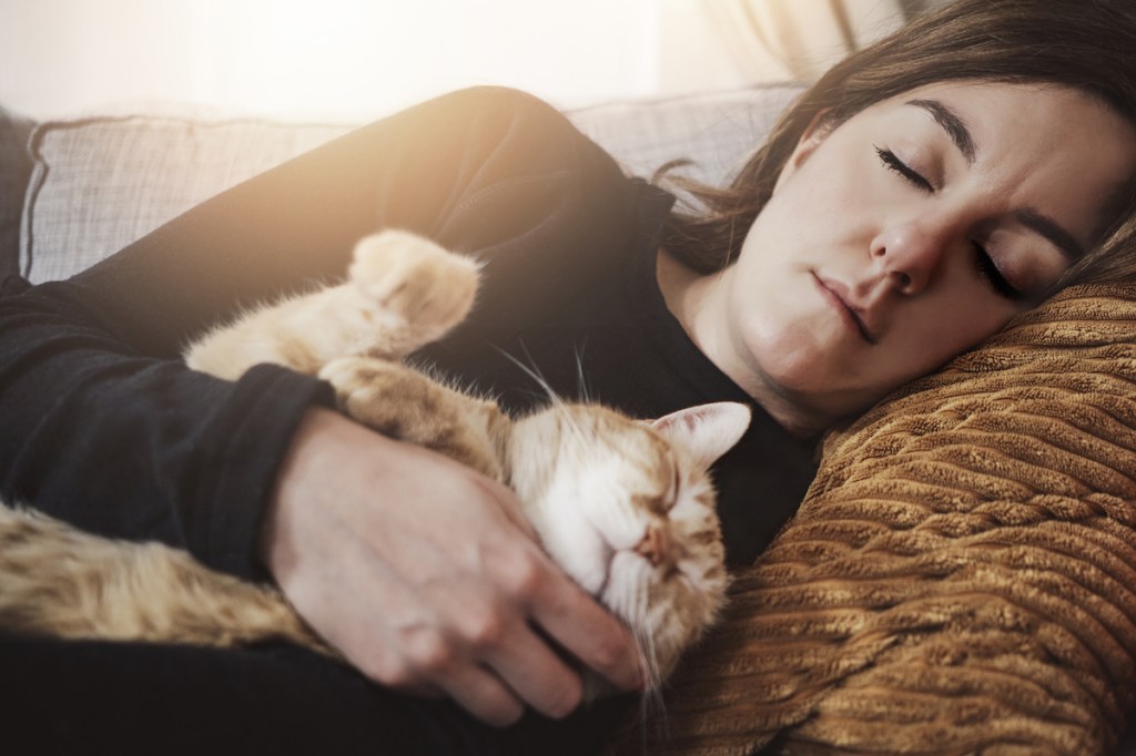 Woman and orange tabby cat sleeping on a sofa