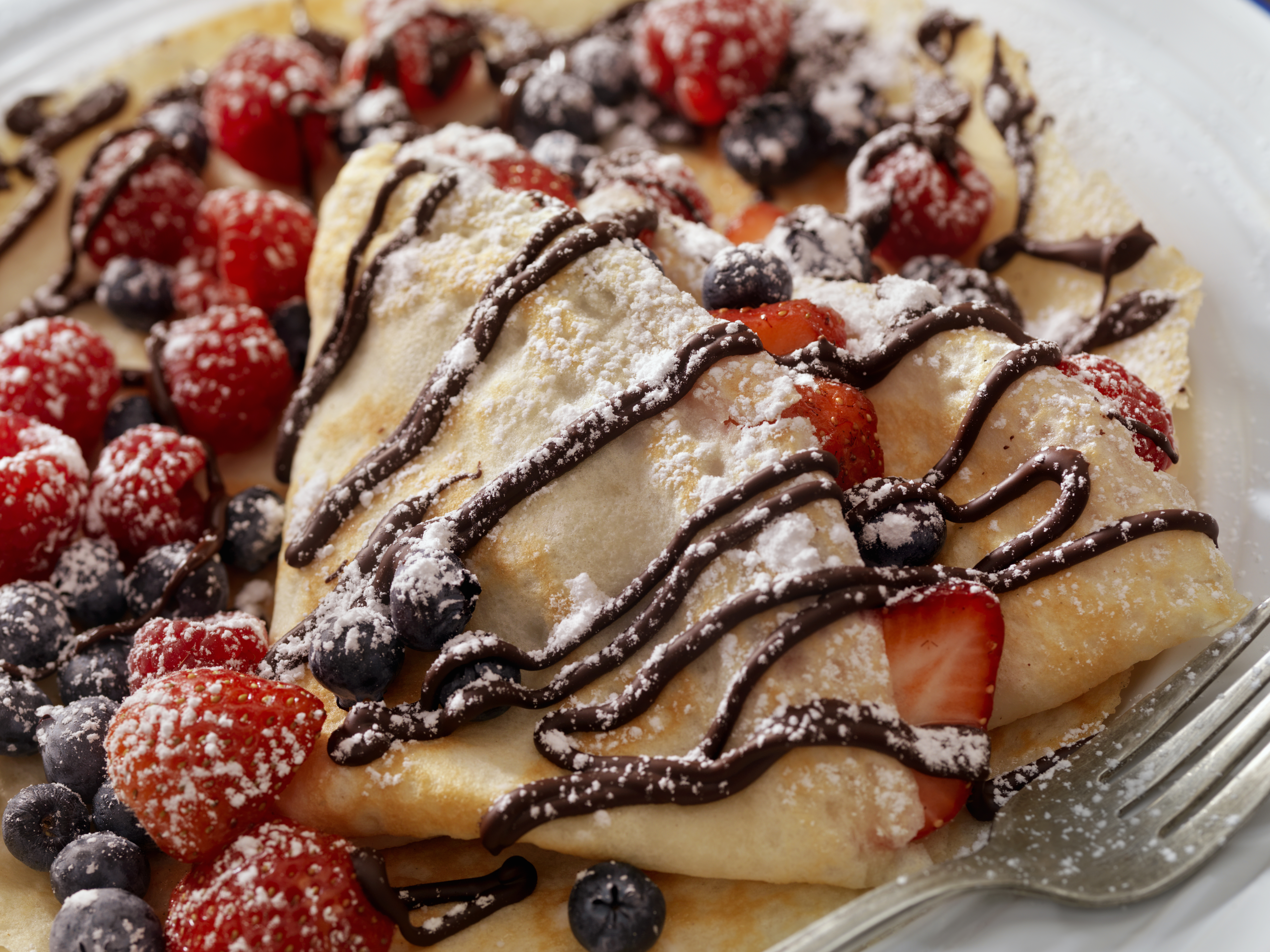 crepe with powdered sugar, chocolate drizzle, and berries