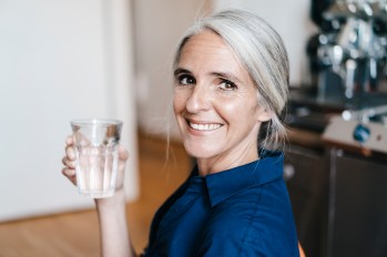 old woman with white hair tied back in a ponytail smiling with glass of water