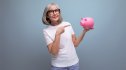 mature woman in tee shirt and jeans pointing at a piggy bank