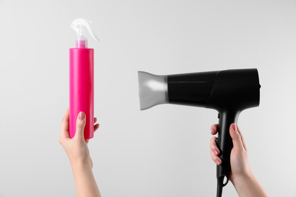 woman holding heat protectant spray and blow dryer