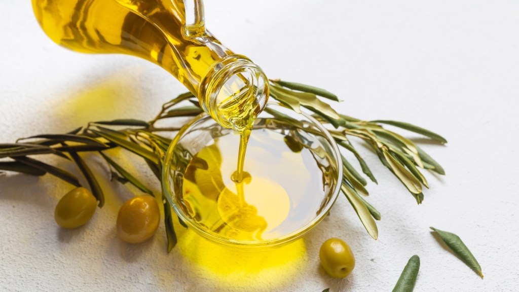 A bottle of olive oil being poured into a glass bowl with olives