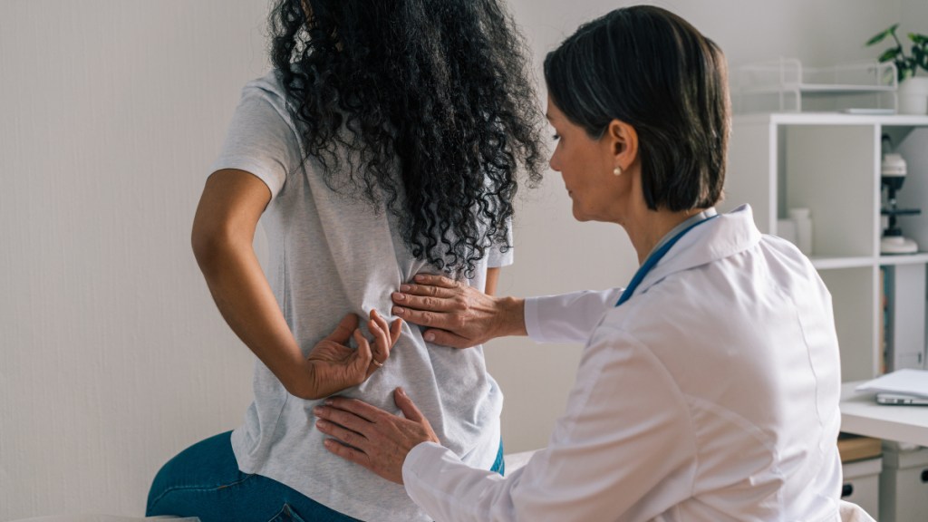 A woman visiting her doctor for lower back self-care as the doctor examines her back in her office