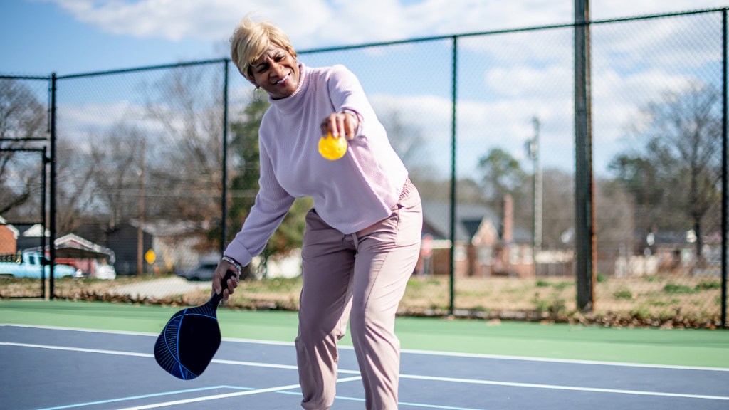 A woman wearing a purple top holding a pickeball and paddle on a court