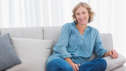 A woman with short hair in a blue shirt relaxing on a couch, who uses holy basil for anxiety