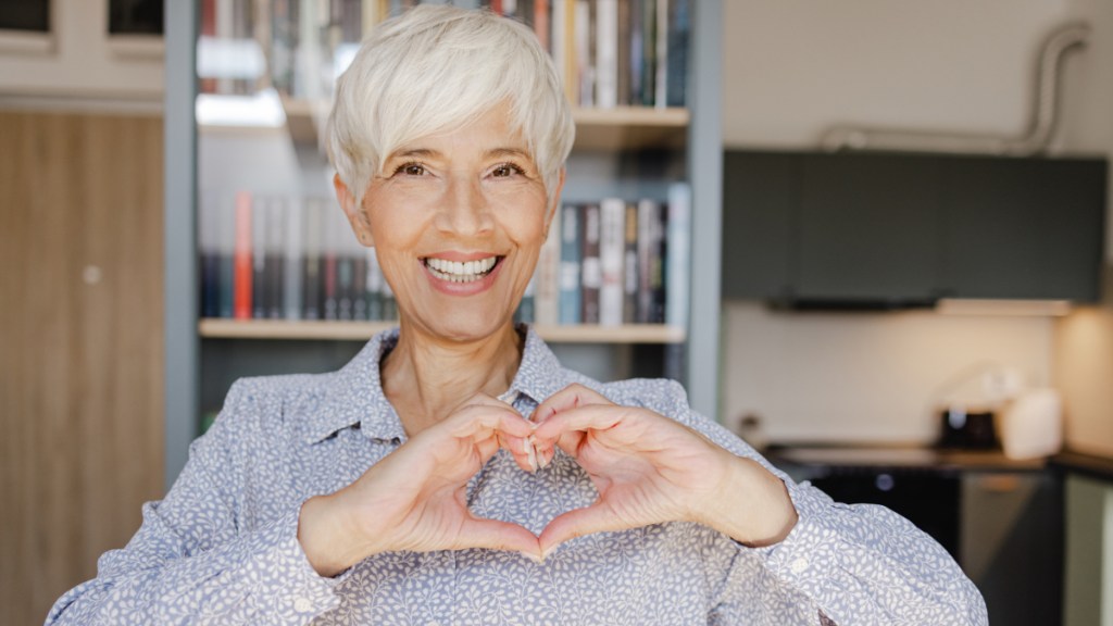 A woman with grey hair making a heart shape with her hands
