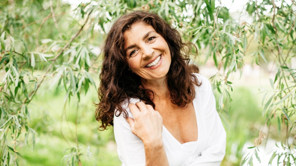 A woman with dark hair in a white top under a tree