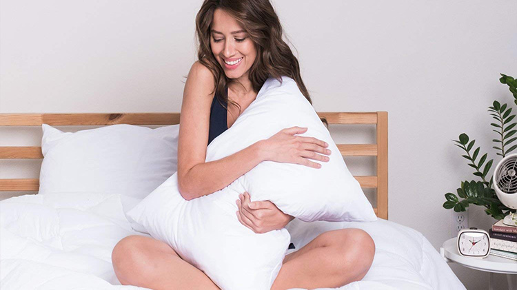 woman sitting on a white bedspread hugging a pillow