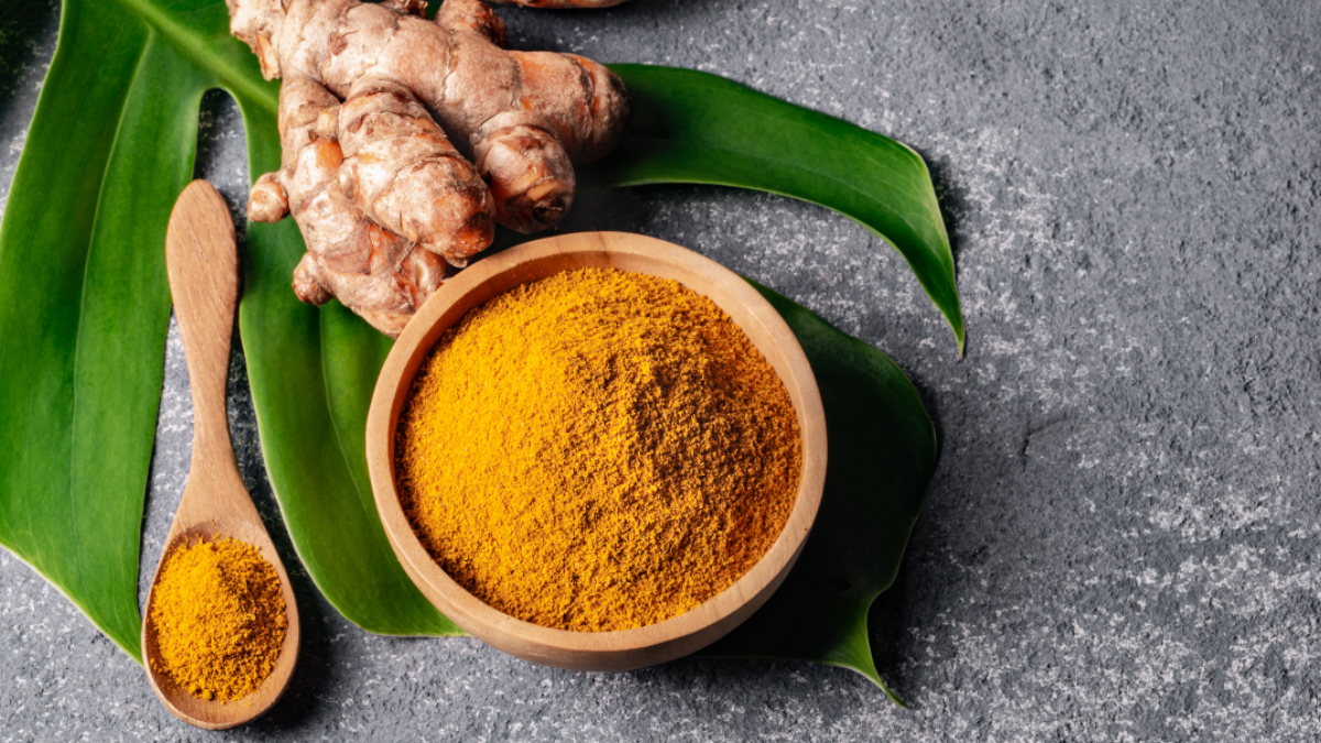 Fresh turmeric root beside a bowl and spoon of ground turmeric, which has many health benefits for women