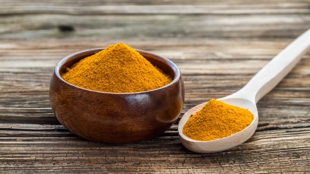 A bowl of ground turmeric next to a spoon of turmeric