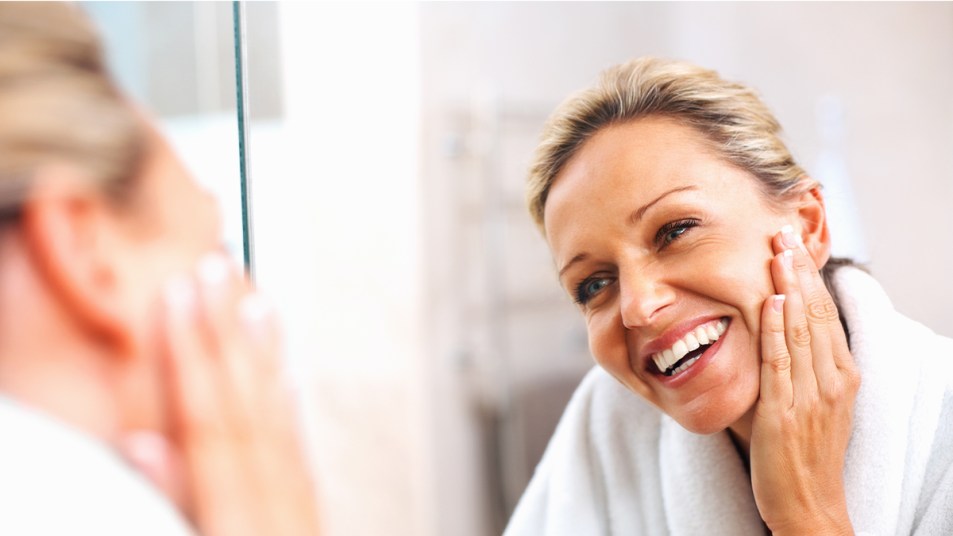 mature woman smiling while doing a face massage in front of the mirror