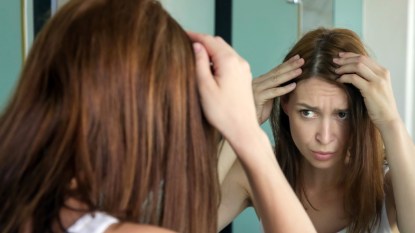 Woman looking at gray hairs in mirror
