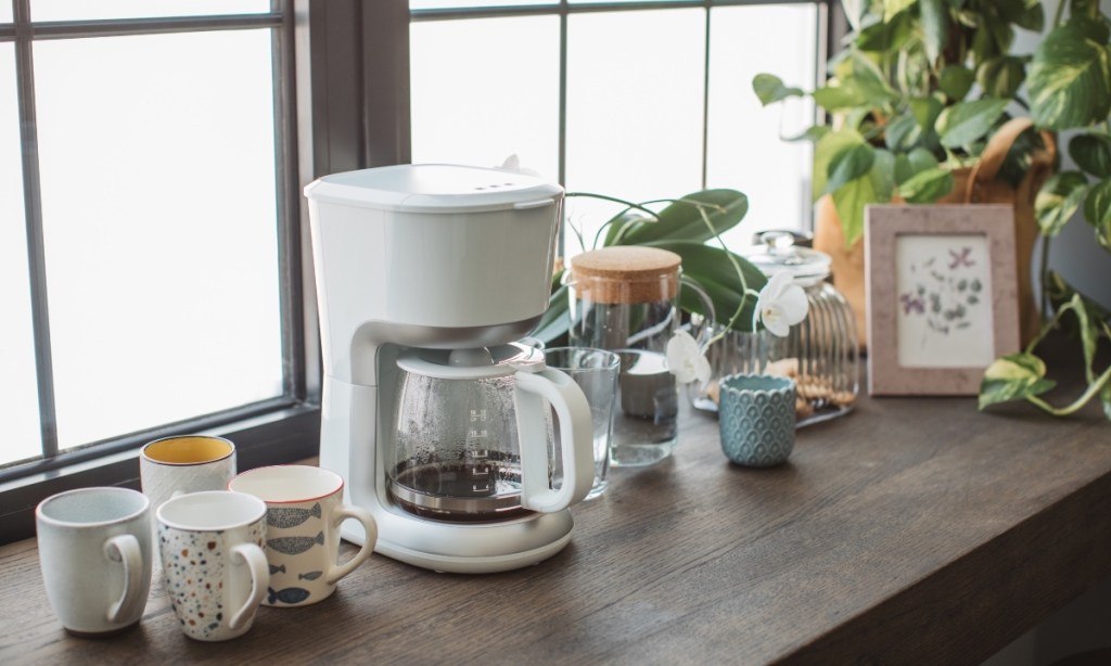 A coffee maker on a countertop with mugs and plants