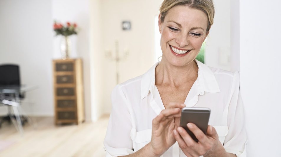 Smiling woman using cell phone at home