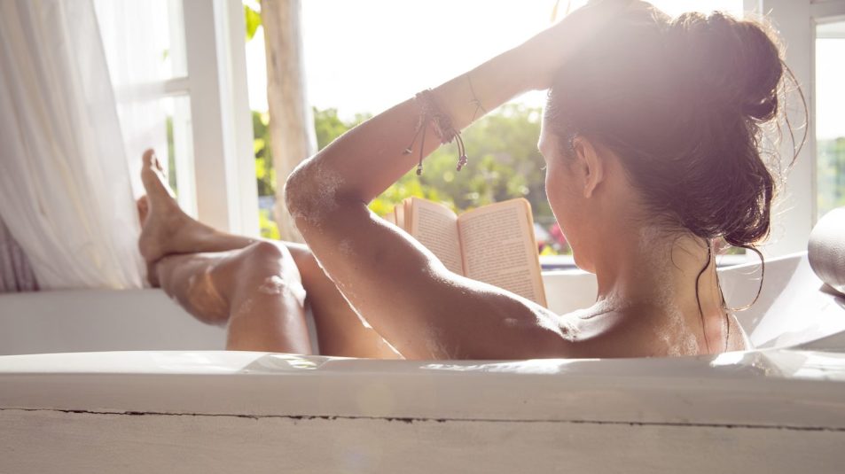 Woman relaxing in bathtub reading book
