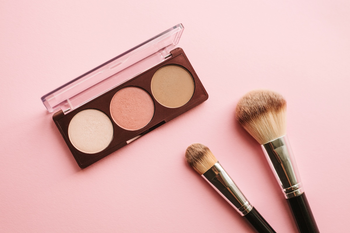 Eye shadow and makeup brushes over pink background.