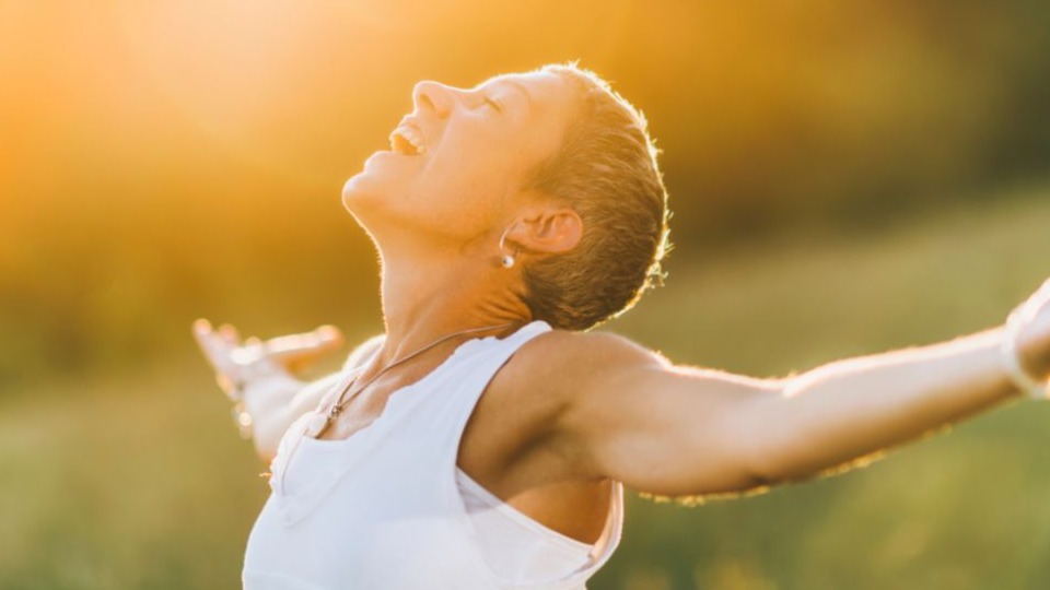 Woman outside with her arms open looking up at sunlight