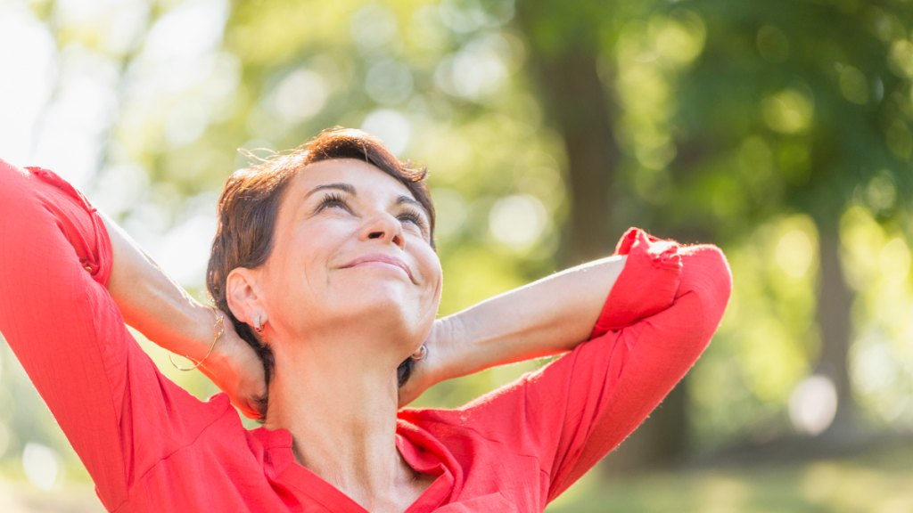 middle-aged woman in nature, looks up toward the sun, happy she is letting go of regret and embracing the future