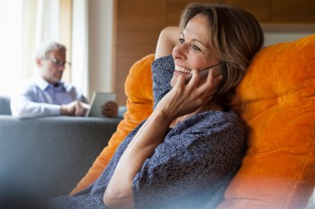 Smiling woman at home on cell phone with husband in background
