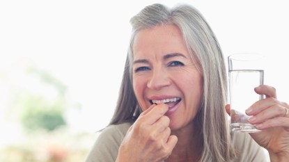 Older woman over 50 taking a vitamin D supplement with a glass of water