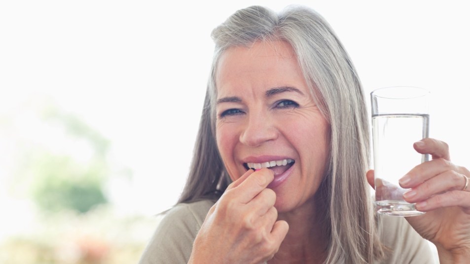Older woman over 50 taking a vitamin D supplement with a glass of water
