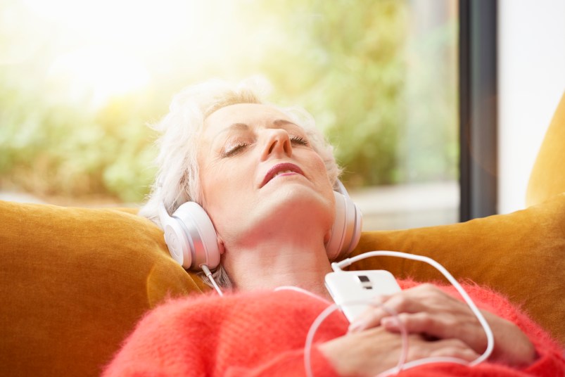 older woman relaxing with music on sofa