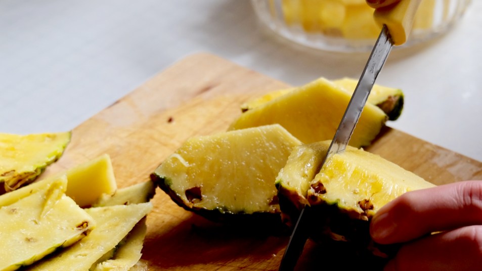 Person slicing pineapple pieces