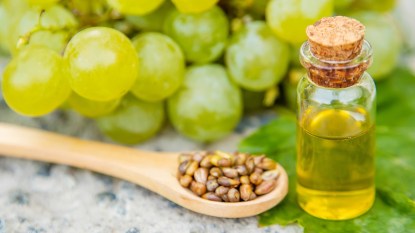 grapeseed oil in a small jar with green grapes in a background and wooden spoon full of grape seeds