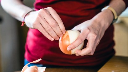 Woman's hands peeling yellow onion