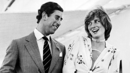 Black and white photo of Princess Diana in a white and floral dress laughing with Prince Charles in a suit at an event before their wedding