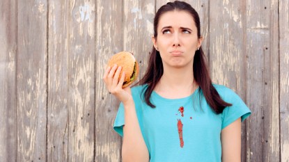 Woman holding burger with ketchup stain on blue shirt