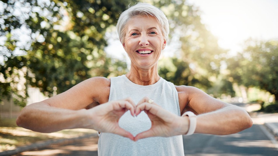 Athletic woman over 50 outside on sunny day making a heart shape with her hands