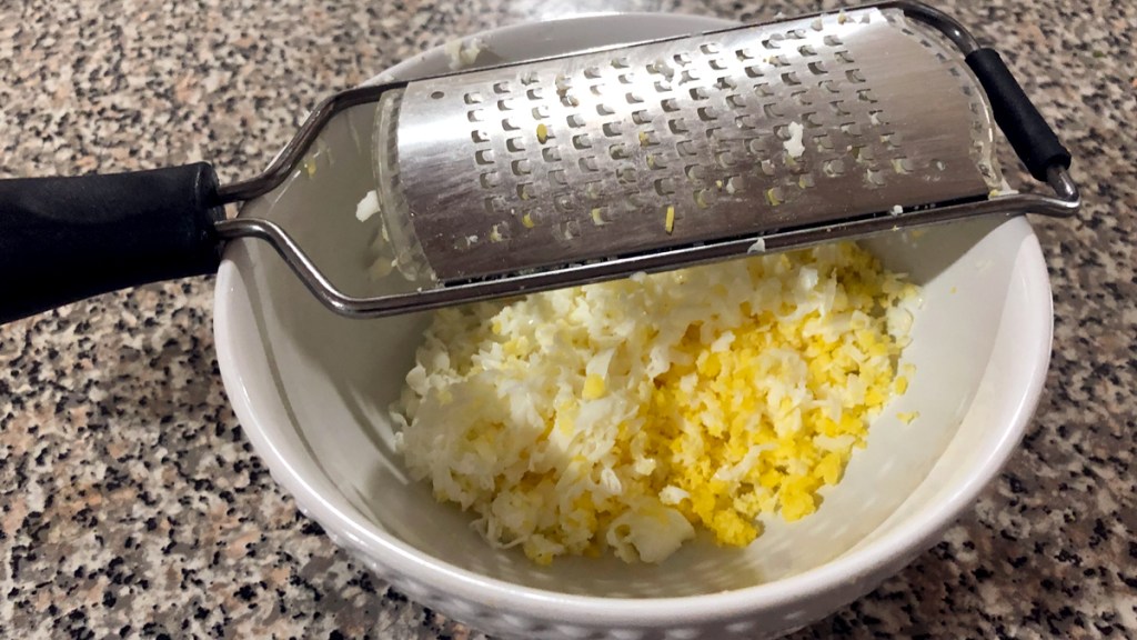 Bowl with a grater on top and grated hard boiled eggs inside