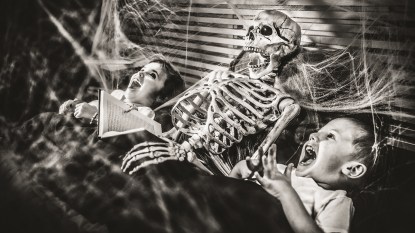A vintage Halloween photo of two children being read a bed-time story by a skeleton