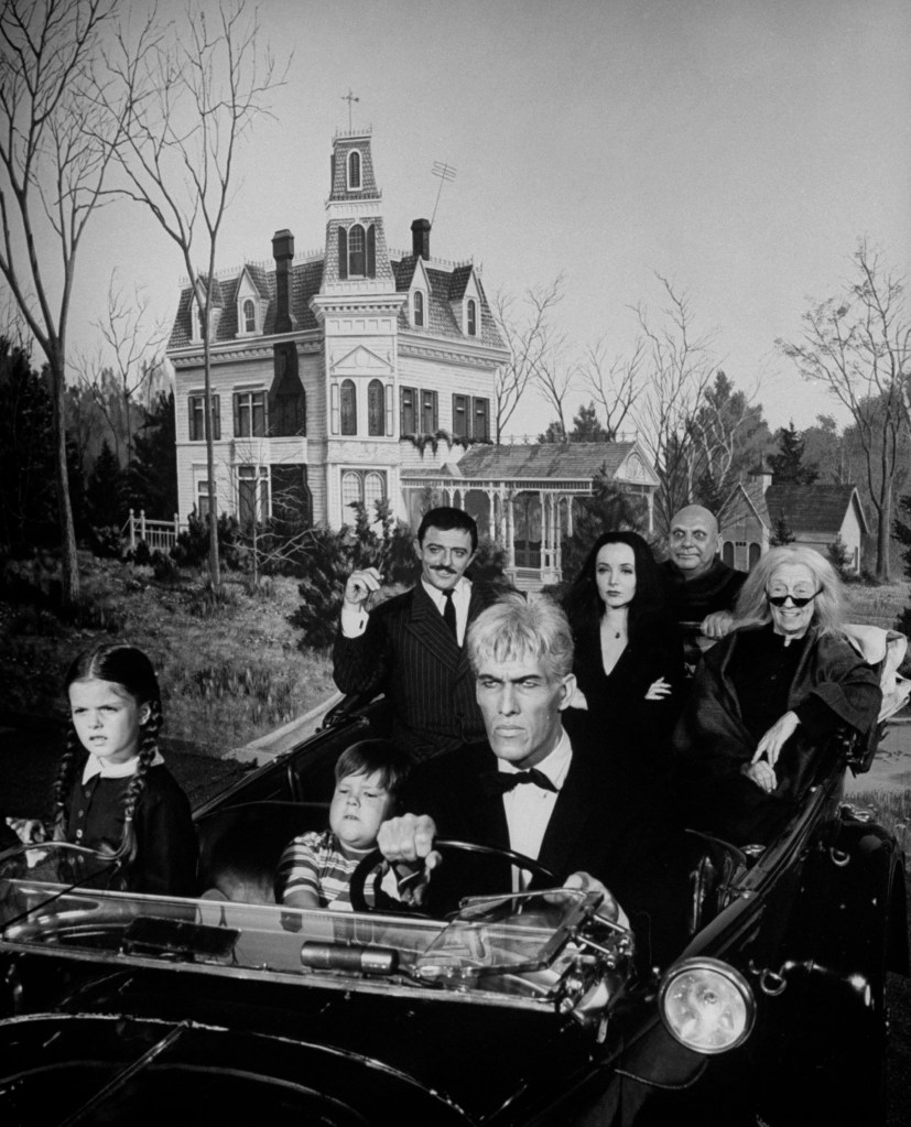 The Addams family riding in old convertible driven by actor Ted Cassidy w. other cast members incl. John Aston (rear-L), Carolyn Jones (rear-C), Blossom Rock (rear-R) & boy & girl actors in front seat w. an overall exterior view of their creepy home in.