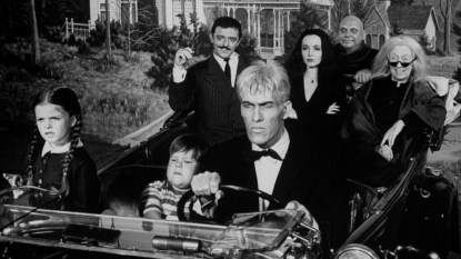 The Original Addams family riding in old convertible driven by actor Ted Cassidy w. other cast members incl. John Aston (rear-L), Carolyn Jones (rear-C), Blossom Rock (rear-R) & boy & girl actors in front seat w. an overall exterior view of their creepy home in.