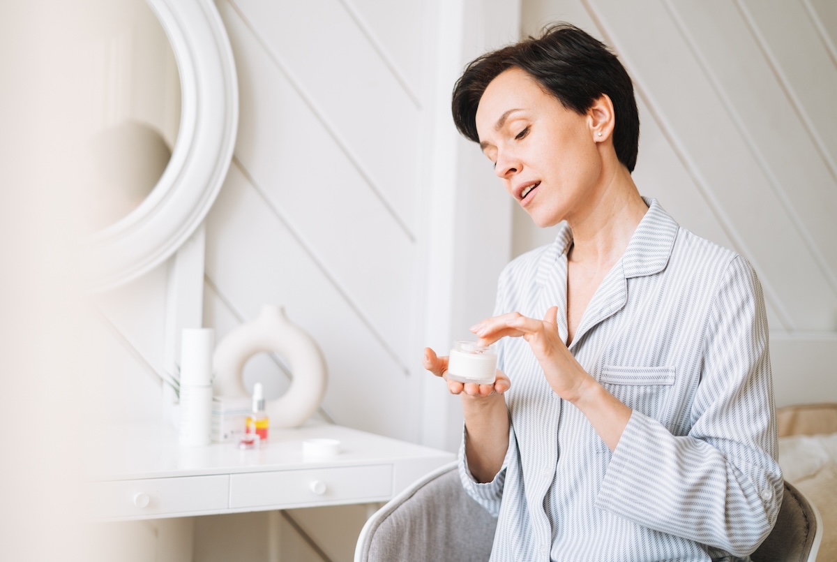 Young adult brunette woman with short hair applies cream to her face at home, morning skincare routine