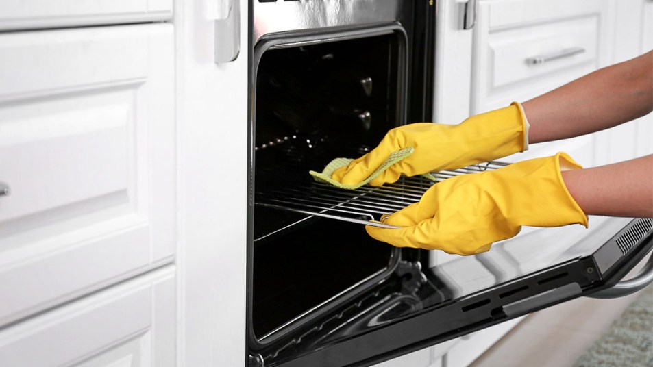 closeup of woman's gloved hands cleaning an oven