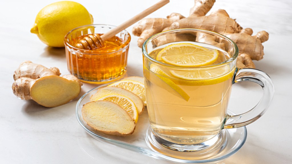 A cup of ginger tea next to honey, fresh lemons and ginger
