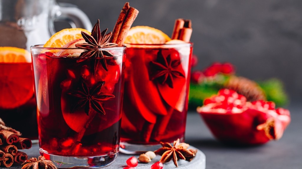Two glasses of red wine and pomegranate juice with star anise, cinnamon and other holiday spices