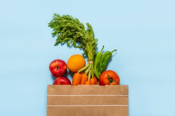 basket of fresh fruit and sugar vegetables like apples and carrots against a blue background
