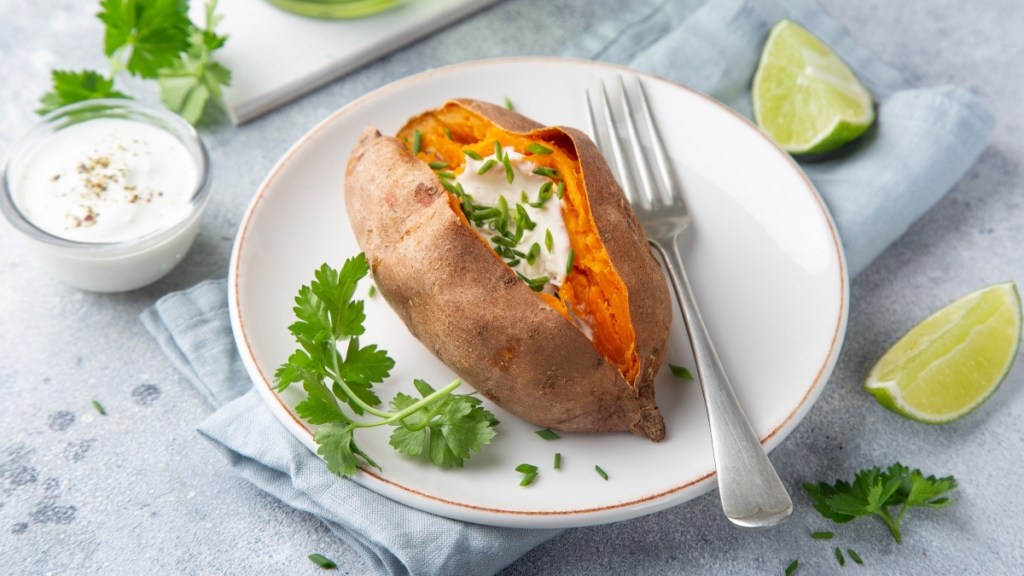 A baked sweet potato topped with yogurt beside lime slices