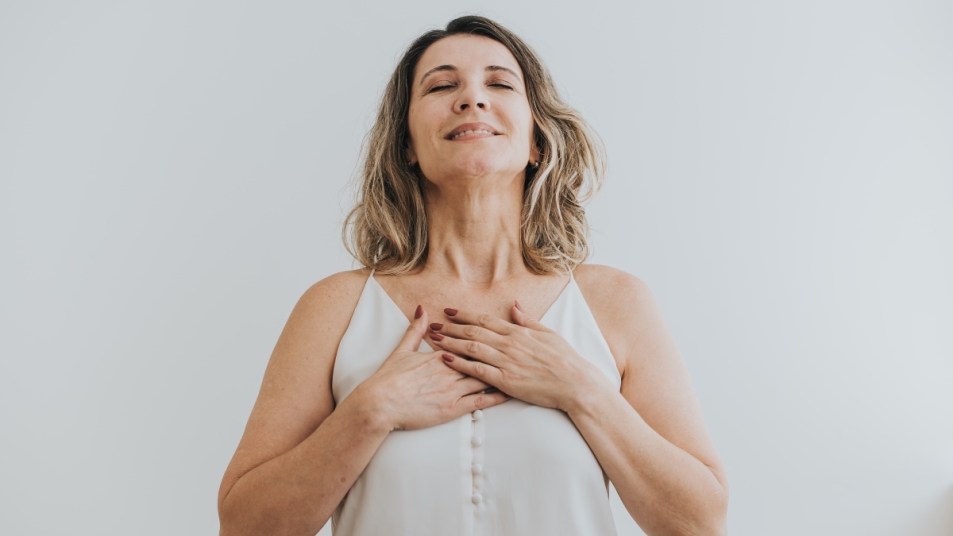 A woman in white top with her hands on her chest, who used fast-acting heartburn relief home remedies